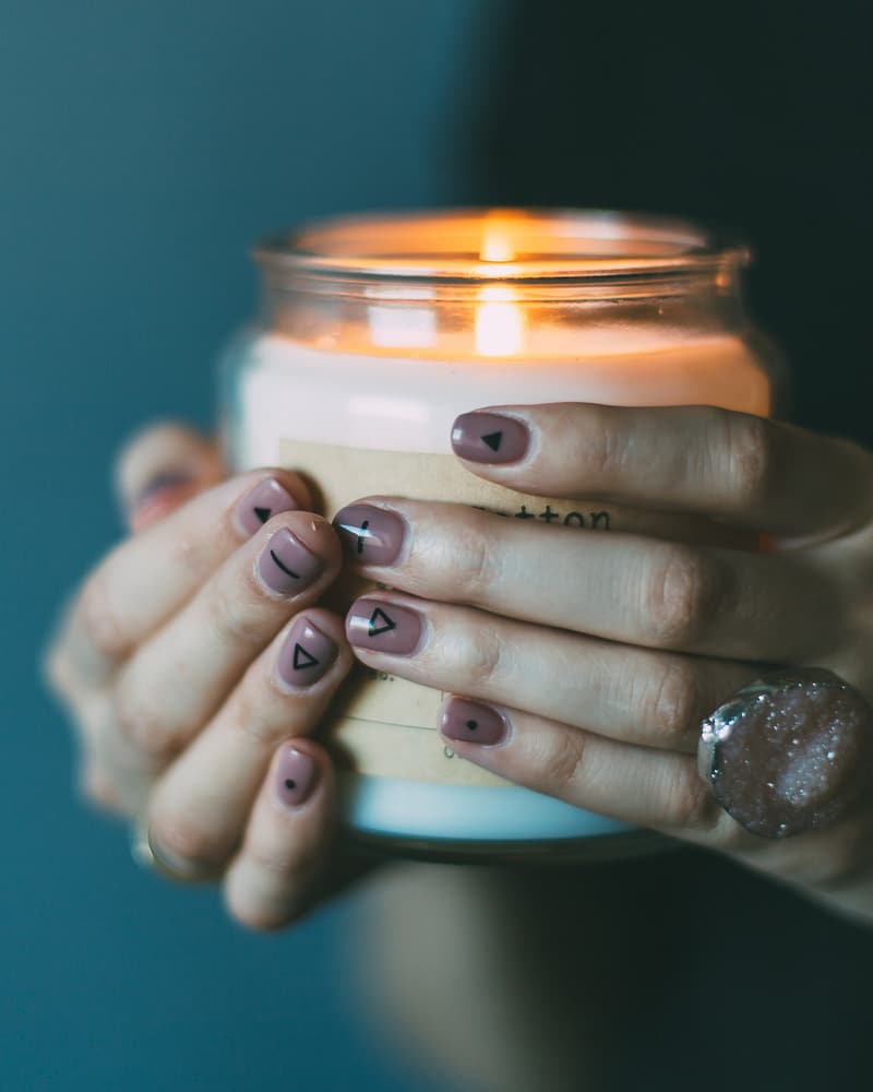 Hands with a dark taupe gel colour holding a lit candle